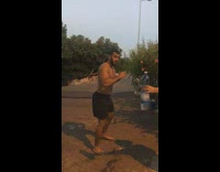 Shirtless guy does bottle cap challenge with blue water bottle, kicks high and falls on dirt ground
