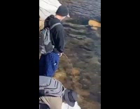 Man fills water while man urinates beside at the river