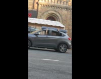 Driver and passengers hold onto mattress on top of car 