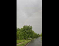 Rainbow arc on cloudy sky trees street