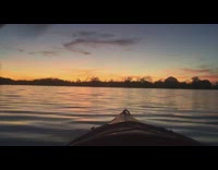 Guy rides brown canoe across lake sunset 