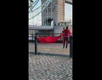 Woman in red dress poses while man waves the end of the dress