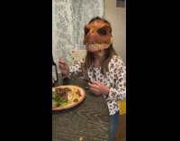 Family eating dinner with dinosaur mask