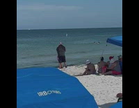 Woman in bikini dances while man films at the beach