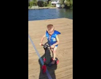 Little boy rides his scooter off the dock and jumps into lake