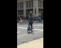 Biker with basketball on head rides with leg out 