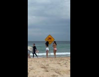Woman in bikini poses beside beach signage