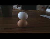 Guy balance white egg over brown egg