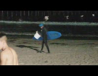 Guy with blue surfboard and hat stretches and wanders around beach 