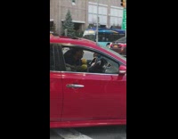 Guy driving red car shakes yellow maracas 