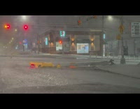 Broken crosswalk sign post fallen onto street in snowstorm 

