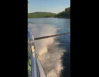 Guy orange vest holds onto pole on boat, gets hit by wave and flies into ocean water
