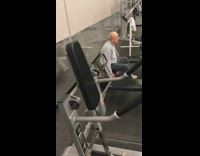 Old man bounces on gray medicine ball at the gym