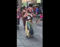 Woman in green dress and messy hair plays electric guitar and sings with open mouth on sidewalk