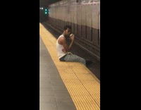 Guy waits for train sitting on edge of platform 