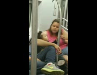 Mother in pink shirt wipes sons nose with a tissue on the subway