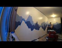 Guy paints blue mountain mural on wall 