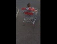 Girl slowly rolls down street in shopping cart hits a curb and falls off