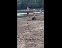 Woman in black dress poses with phone on tripod at the beach
