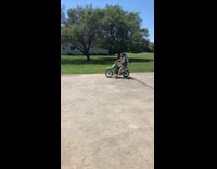Guy with blue beach folding chair on his back does a wheelie on green dirtbike and falls back