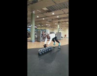 Guy uses ab wheel across line of kettlebells 