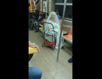 Old woman in wedding dress veil sits on subway with rolling cart
