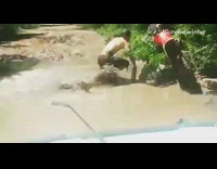 Guy rides motorcycle down muddy road, falls into giant mud puddle