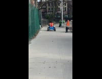 Guy rides blue toy car down sidewalk 