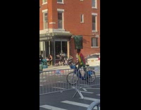 Guy rides bicycle and balances trash can 