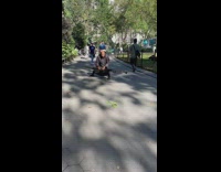 Man in robe balancing book on head waving pole around on sidewalk