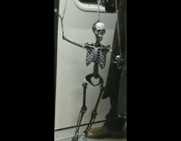 Man in black coat hat makes skeleton puppet dance on subway train