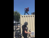 Spiderman on top of crate yiking in front of bycycle cop