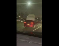 Red minivan drives with mattress on roof 