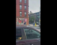 Guy riding bike balancing a giant present on his head in the street 

