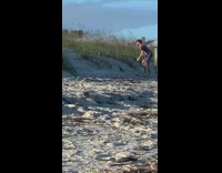 Guy bottle on sand woman stand windy