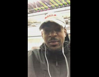 Man wears blue durag, two hair picks, and long purple coat, and sings loudly on subway train