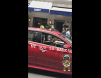 Man plays yellow maracas while driving in red car
