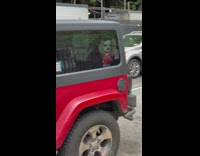 Red jeep has clown hiding in the back staring out the window 