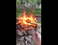 Filmer picks up stick throws in campfire