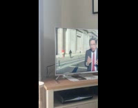 Woman in red top poses behind the news reporter on TV Part 1