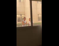 Two ladies jump pose outside apartment window 