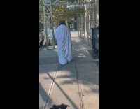 Person wears bedsheets on sidewalk 