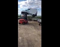 Red forklift lifts white van on forks and drops it on the ground in junkyard