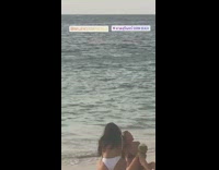 Woman holds coconut takes picture at beach