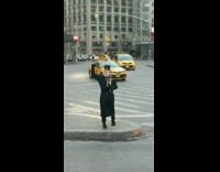 Priest holds Jesus crucifix on sidewalk, fist in the air