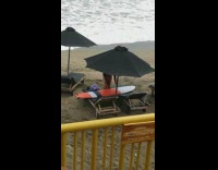 MUSIC girl waxing orange surfboard under black umbrella