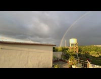 Full rainbow behind person filming sunset rooftop