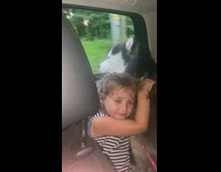 Little girl hugs husky dog car window 