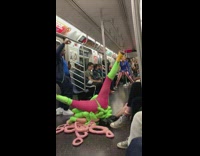 Woman in neon pink and green tentacle costume rolls around on subway floor