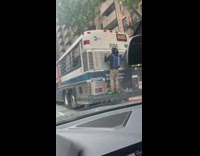 Two guys hold onto back of moving bus